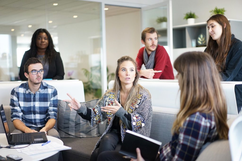 business meeting with a woman talking at the meeting and other employees sitting around her listening