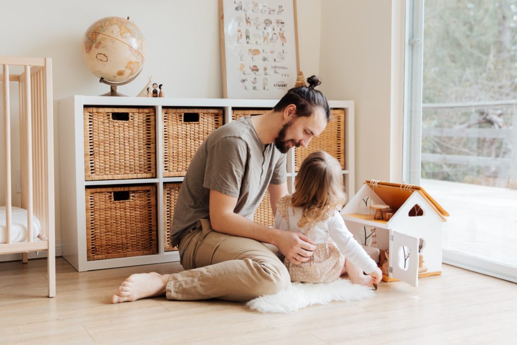father and daughter sitting on the floor in the bedroom playing with a dollhouse