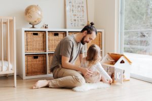 father and daughter sitting on the floor in the bedroom playing with a dollhouse