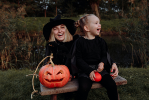 mom and daughter laughing dressed for halloween with carved pumpkin in field