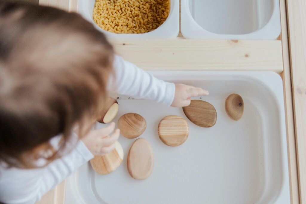 A toddler playing with wooden stones in a Montessori educational setup, promoting motor skills development.